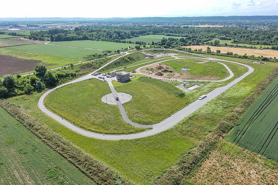 Aerial view of the Test Arena in Linz, featuring a paved circular track, a rough-road test area, a noise measurement station, and test areas set amid a sprawling green landscape.