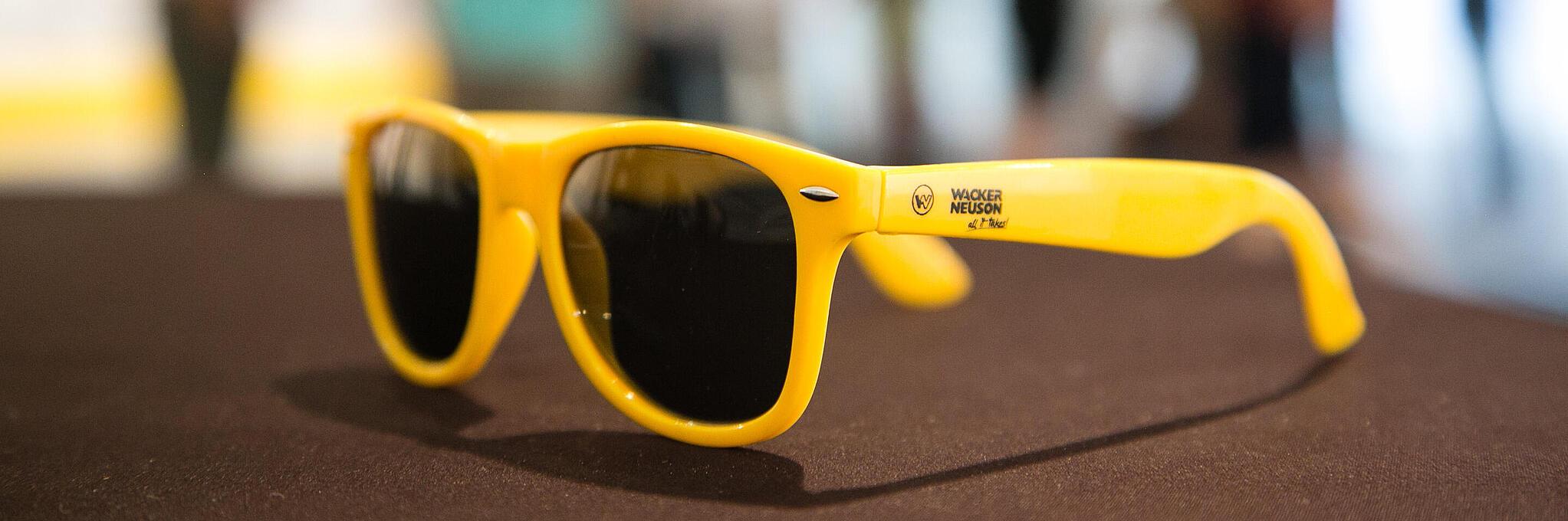 Yellow sunglasses with Wacker Neuson logo.